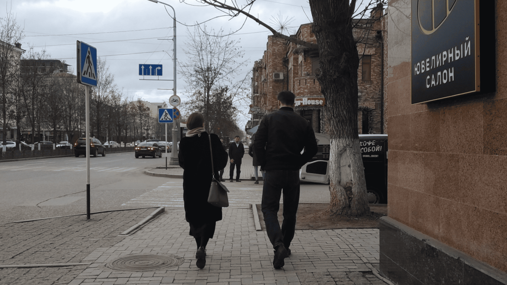 Couple walking along a street in Grozny with brick buildings and Russian signage