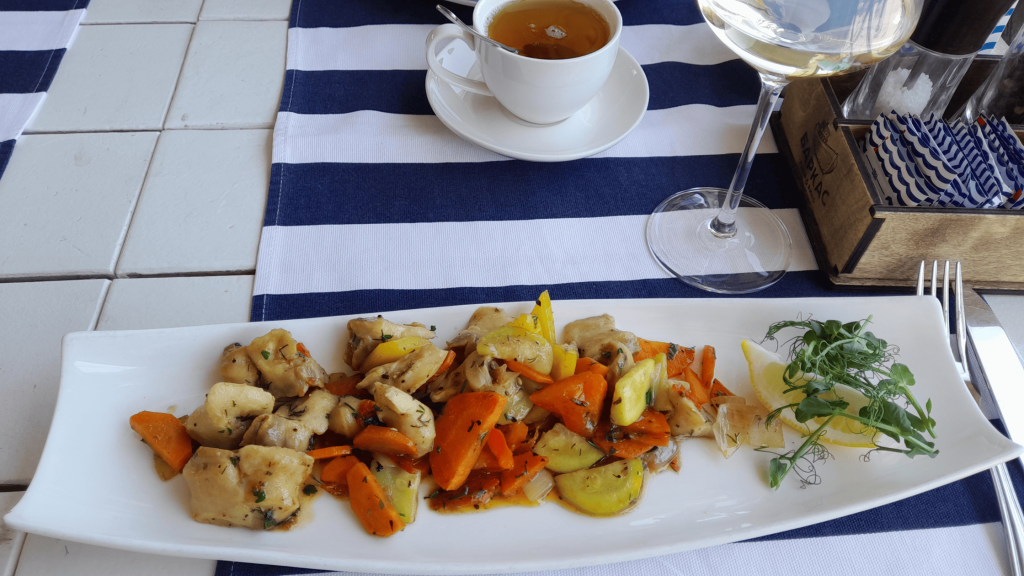 Plat de rapanas sautées avec légumes colorés servi avec un verre de vin blanc en Crimée
