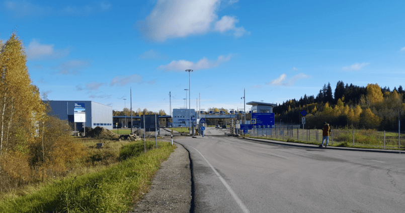 Photo du poste-frontière de Luhamaa reliant l’Estonie à la Russie, entouré de feuillage d’automne sous un ciel bleu clair.
