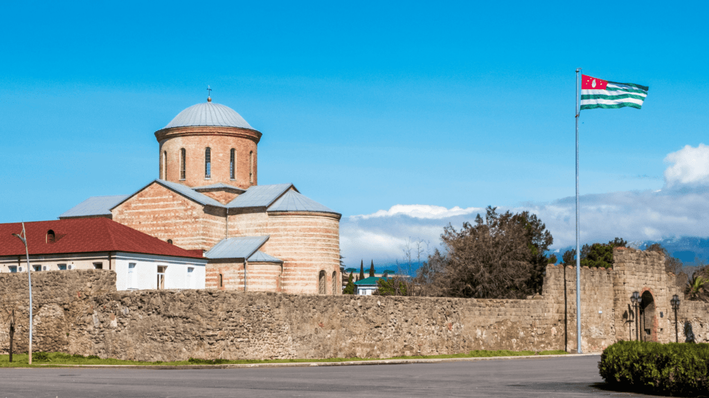 The Pitsunda Cathedral in Abkhazia, surrounded by stone walls and featuring an Abkhazian flag