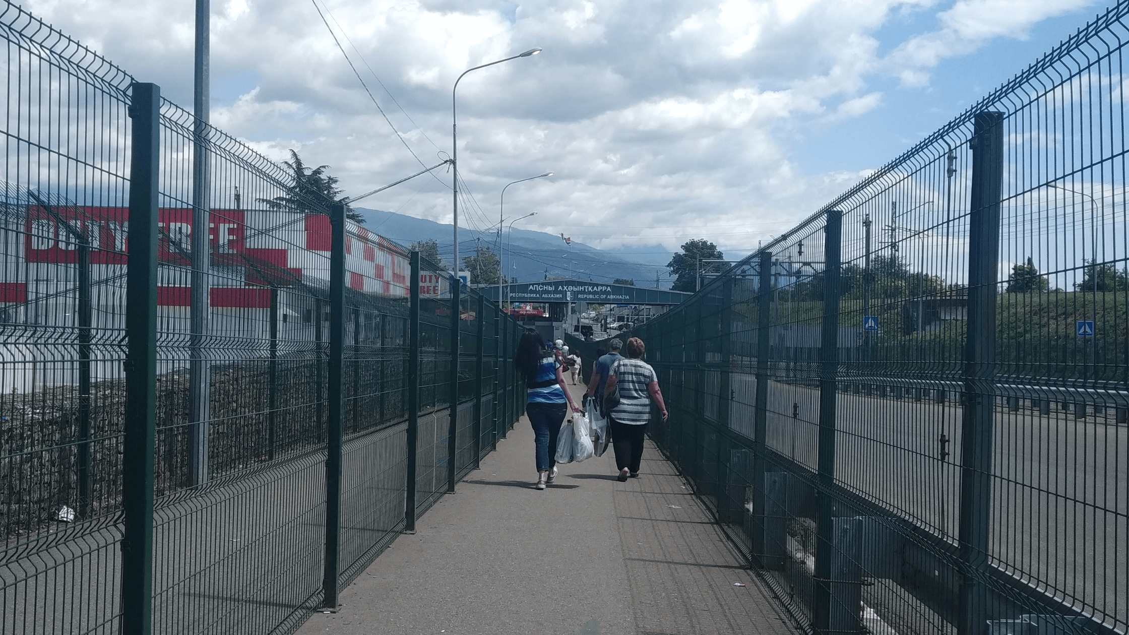 Travelers crossing the Psou border between Russia and Abkhazia on foot under a partly cloudy sky