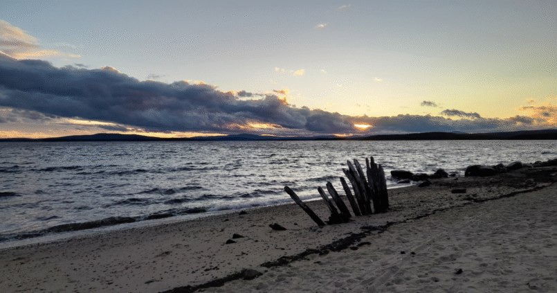 Sunset over the White Sea in Kandalaksha, Kola Peninsula, with calm waves and wooden posts on a sandy shore