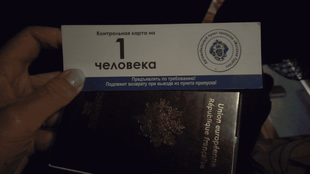 Control card for one person issued at the Donetsk checkpoint, held above a French passport inside the bus.