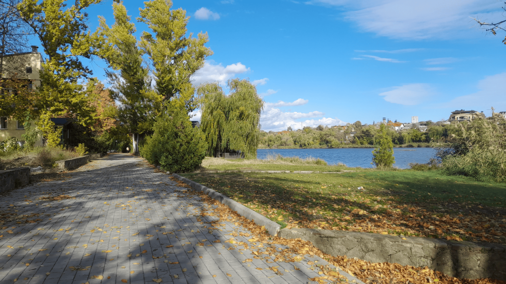 Autumn view of the Kalmius River embankment in Donetsk with yellow trees, a paved walkway, and calm blue water in 2025.