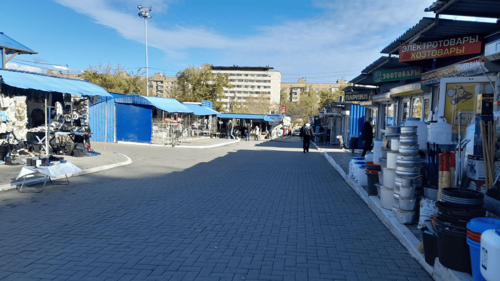 Outdoor local market in Donetsk with blue-roofed stalls selling clothes and household goods on a sunny day in 2025.