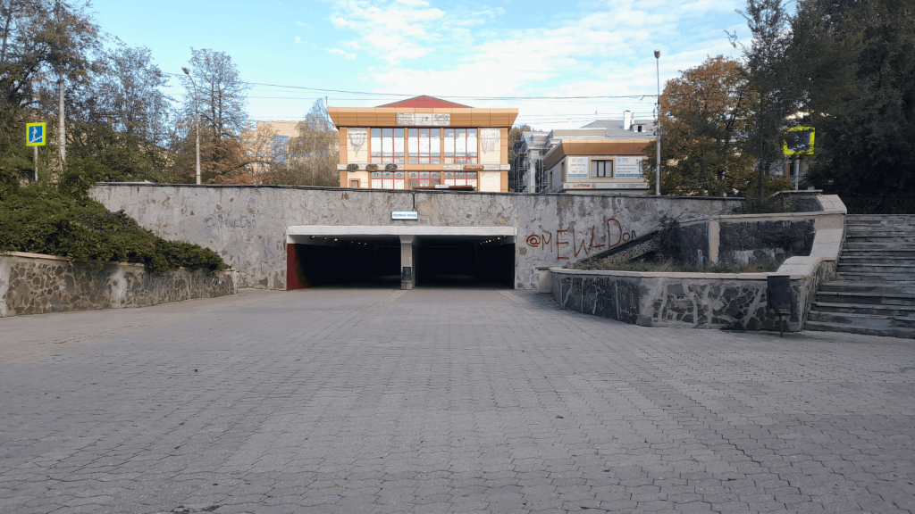 Entrance to a pedestrian underpass in Donetsk with two tunnel openings, stone walls, and a building in the background.