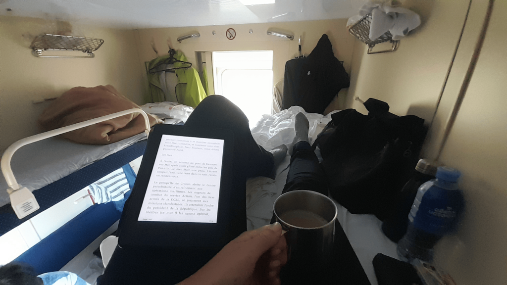 Solo female traveler relaxing in a women-only carriage on the Trans-Siberian sleeper train with ebook and tea