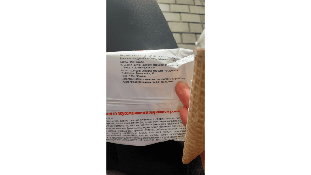 Gros plan sur l’emballage d’un produit indiquant une fabrication au Donbass, avec une main tenant une gaufrette glacée.