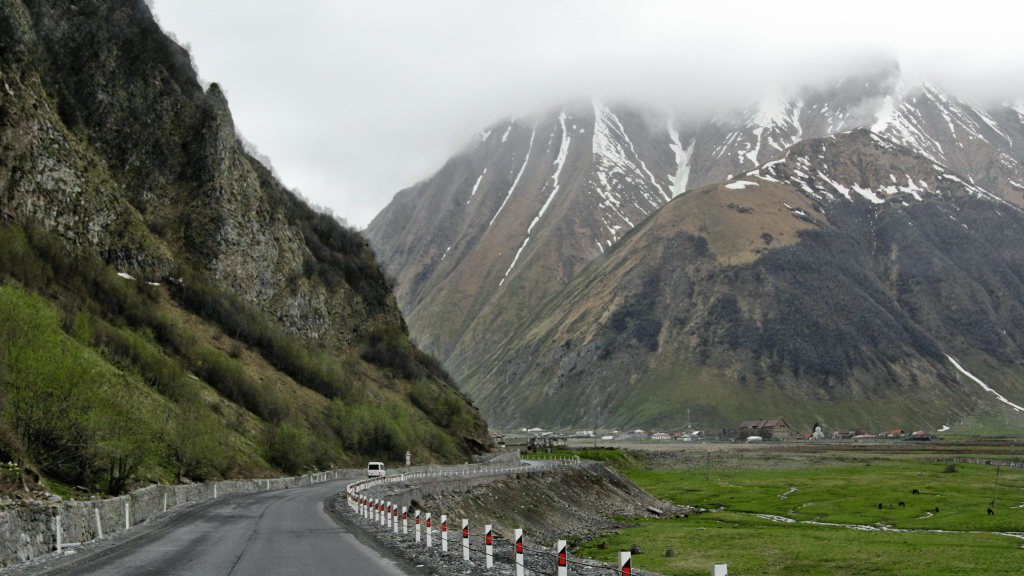 Route militaire géorgienne près de Kazbegi avec montagnes enneigées et vallée verte avant la frontière Russie–Géorgie