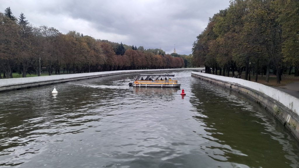 Boat on the Svislach River in Minsk during early autumn, with trees showing seasonal colors.