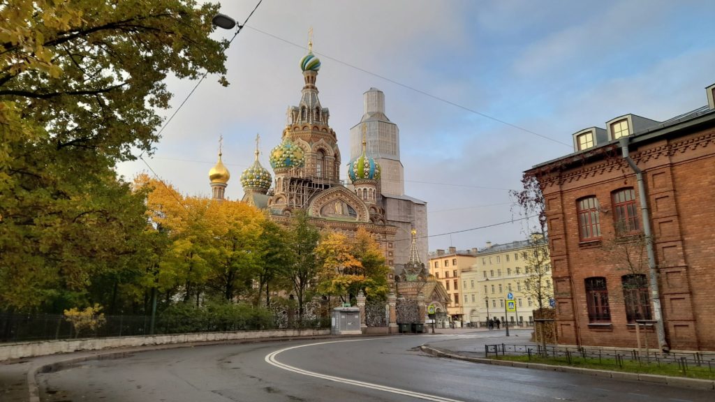 Église du Saint-Sauveur-sur-le-Sang-Versé à Saint-Pétersbourg vue depuis le canal avec des arbres d’automne et une architecture historique.